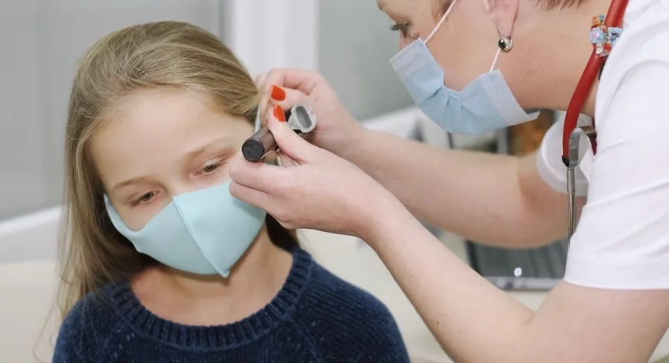 A woman wearing a mask is getting her ear examined.