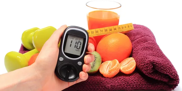 A person holding a glucose meter in front of some fruit.