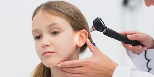 A person is using an ear otoscope on a young girl.
