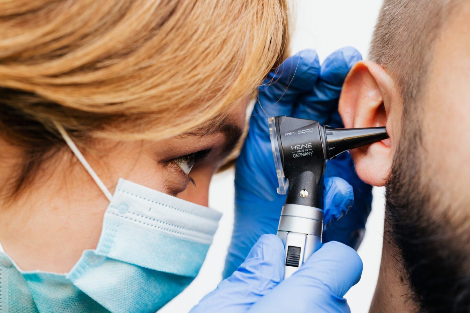 A person wearing blue gloves and an ear protractor.