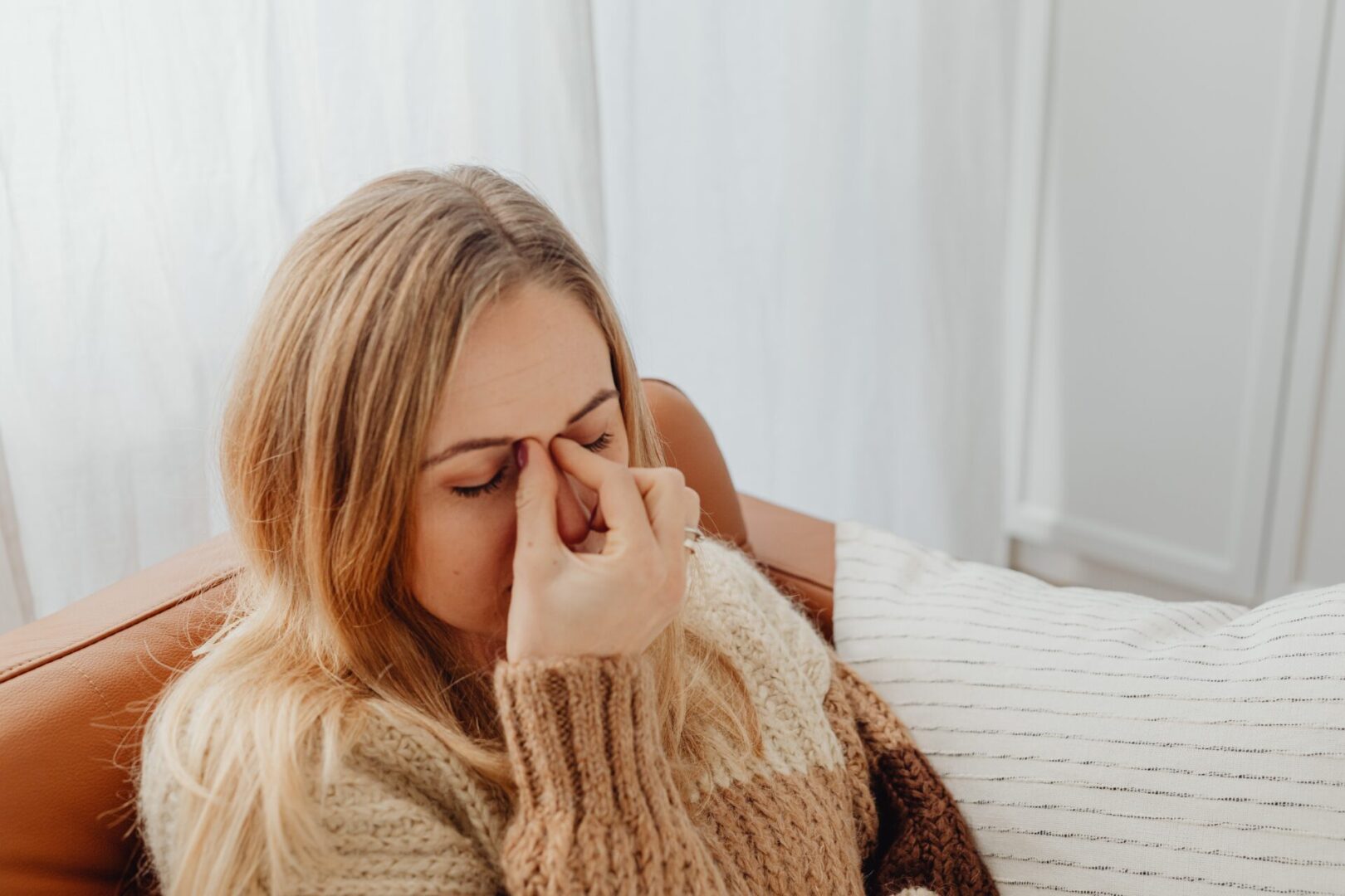 A woman sitting on the couch rubbing her nose.