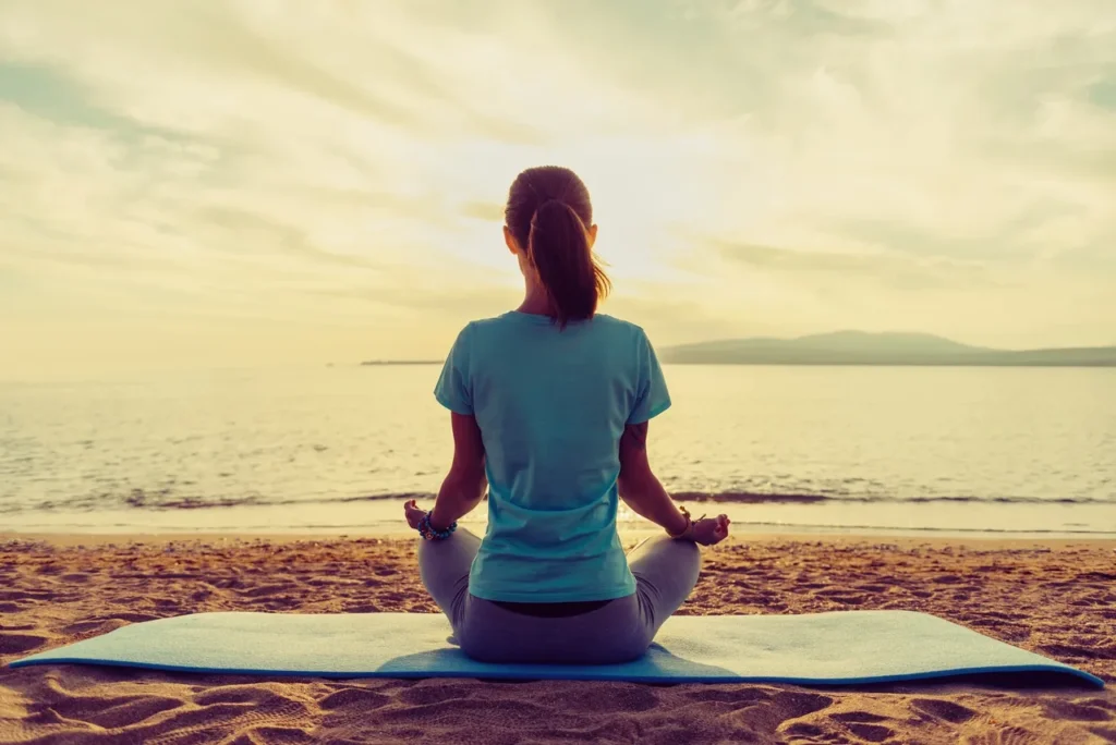 A woman sitting on the beach in front of water.