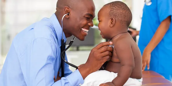 A doctor is holding a baby and smiling.