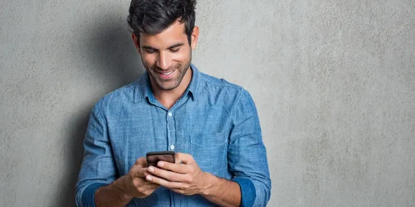 A man is smiling while looking at his phone.