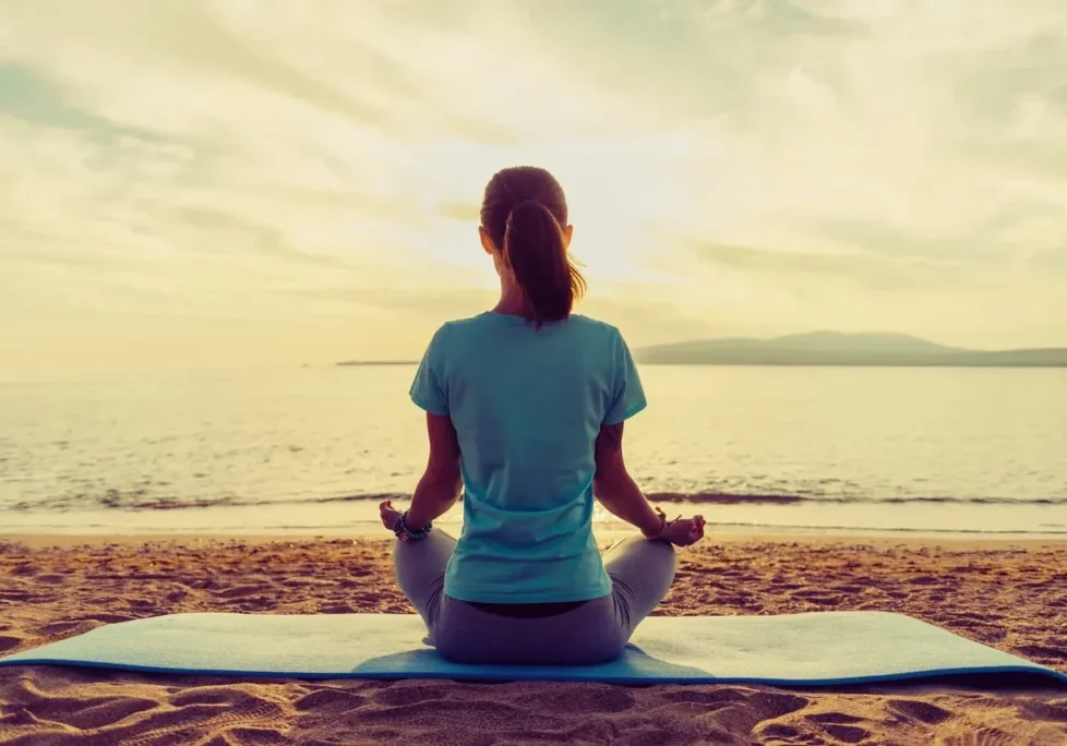 A woman sitting on the beach in front of water.